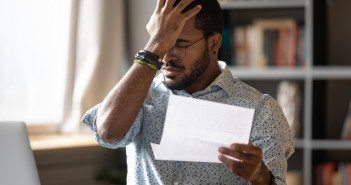 Stressed,African,Businessman,Sit,At,Desk,Hold,Paper,Letter,Reading