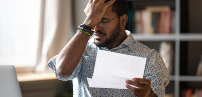 Stressed,African,Businessman,Sit,At,Desk,Hold,Paper,Letter,Reading