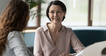 Two,Female,Business,Colleagues,Of,Different,Ages,Chatting,At,Workplace