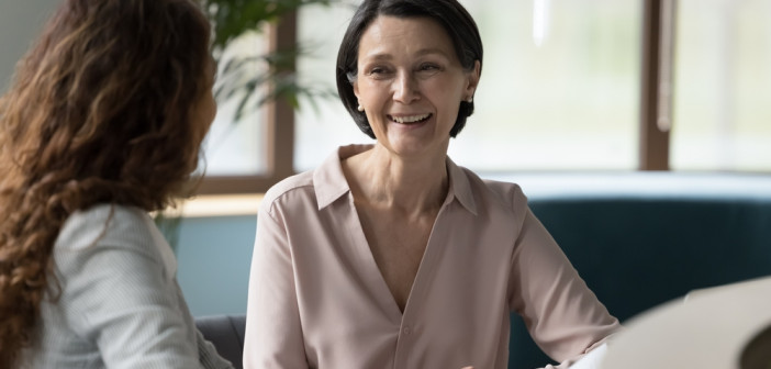 Two,Female,Business,Colleagues,Of,Different,Ages,Chatting,At,Workplace