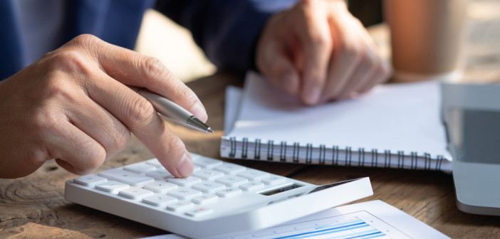 Close,Up,Businessman,Hand,Using,Calculator,And,Working,With,Laptop