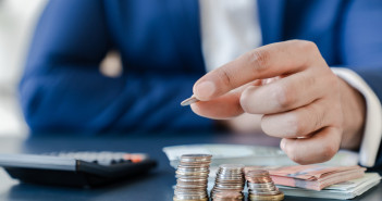 Businessman,Holding,Euro,Cents,Coins,Dollar,Bills,On,Table,With