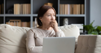 Pensive,Middle-aged,Woman,Sit,On,Couch,In,Living,Room,Using