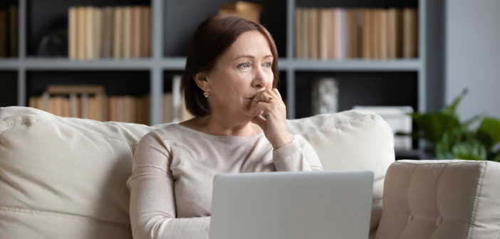 Pensive,Middle-aged,Woman,Sit,On,Couch,In,Living,Room,Using