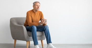 Mature,Man,Drinking,Coffee,Sitting,On,Chair,In,Living,Room.